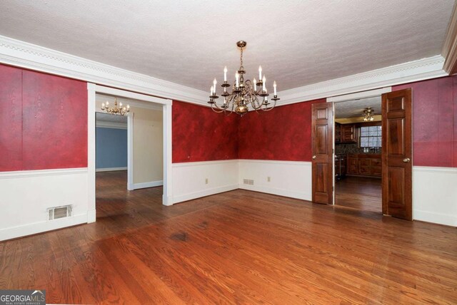 unfurnished dining area with a notable chandelier, ornamental molding, dark wood-type flooring, and a textured ceiling