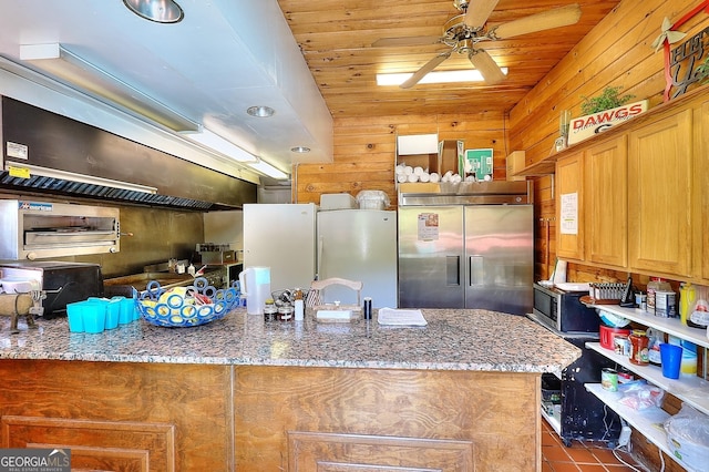 kitchen featuring wood walls, refrigerator, dark tile patterned floors, stone countertops, and stainless steel built in refrigerator