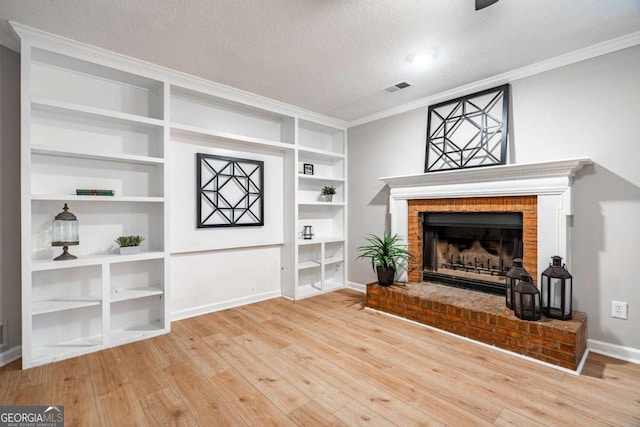 living room featuring built in shelves, a textured ceiling, crown molding, wood-type flooring, and a fireplace