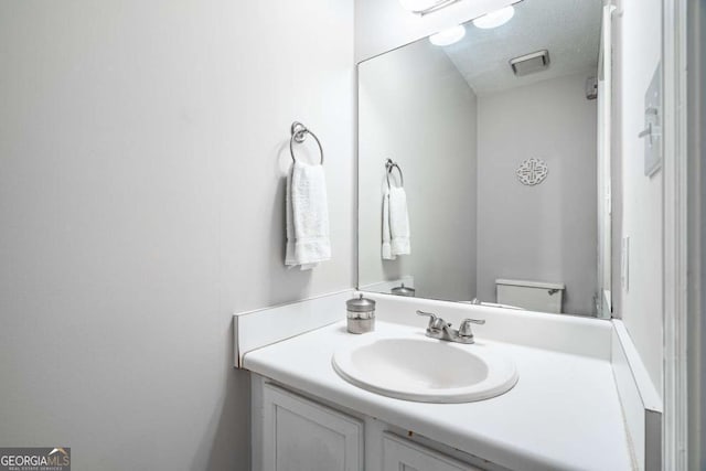 bathroom with a textured ceiling, vanity, and toilet