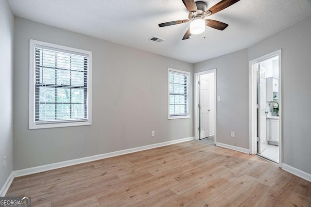 unfurnished bedroom featuring ceiling fan, light hardwood / wood-style floors, connected bathroom, and multiple windows