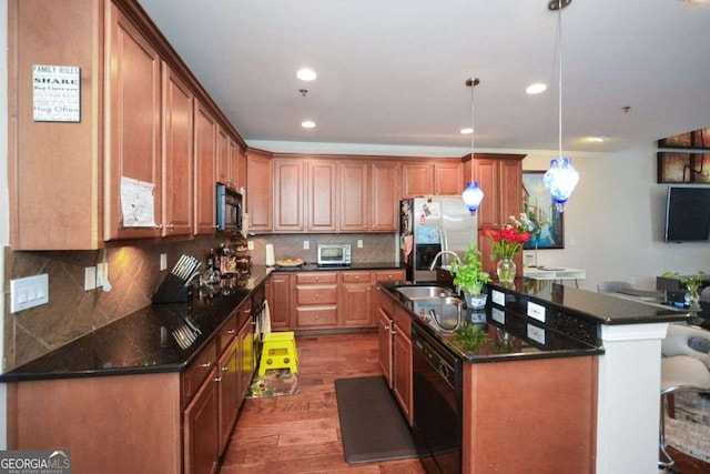 kitchen with dark hardwood / wood-style flooring, a kitchen island with sink, sink, black appliances, and pendant lighting