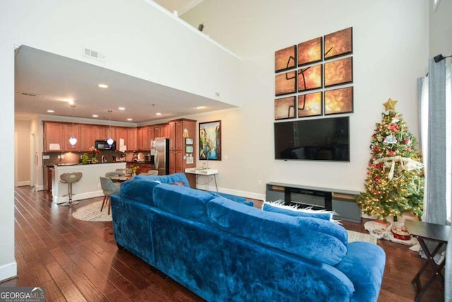 living room with a towering ceiling and dark wood-type flooring