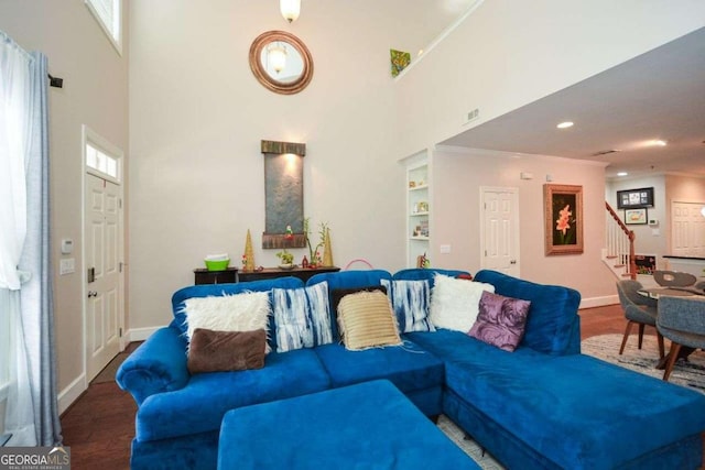 living room with wood-type flooring, built in features, ornamental molding, and a high ceiling