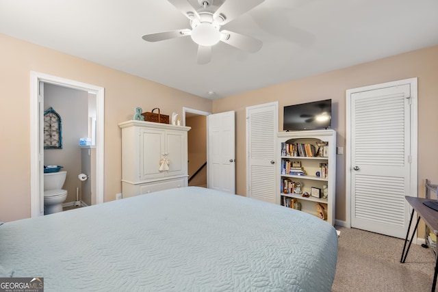 bedroom with connected bathroom, ceiling fan, light colored carpet, and two closets