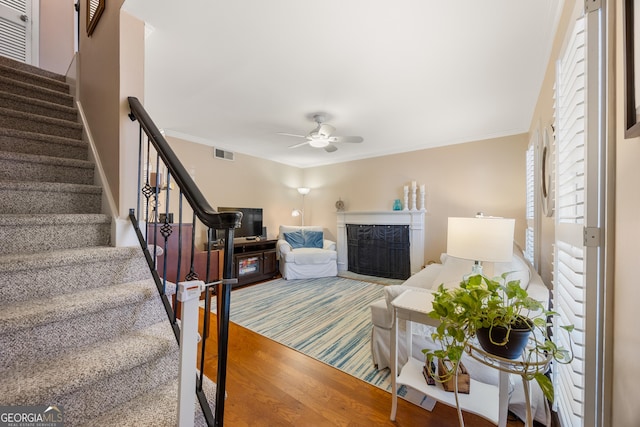 living room with a premium fireplace, hardwood / wood-style floors, ceiling fan, and crown molding