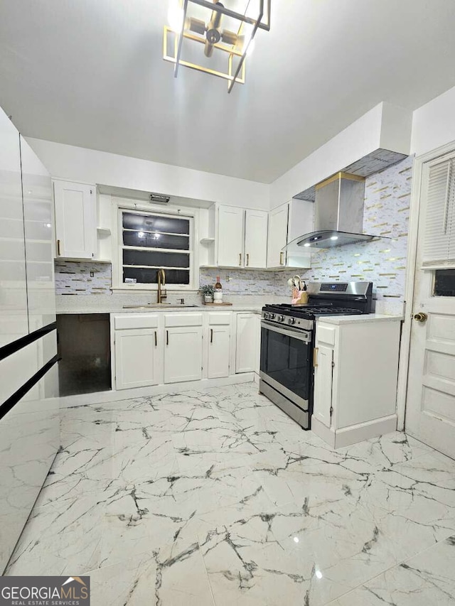 kitchen featuring sink, wall chimney exhaust hood, stainless steel gas range, decorative backsplash, and white cabinets