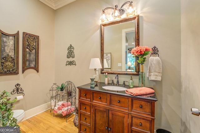 bathroom featuring wood-type flooring, vanity, toilet, and crown molding