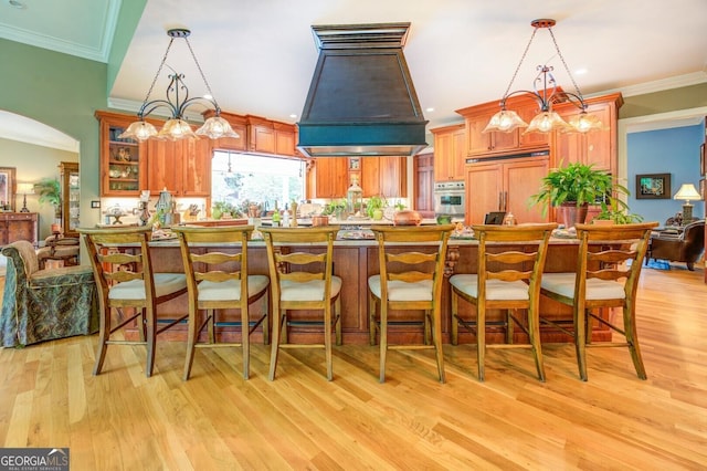 kitchen with paneled built in refrigerator, light wood-type flooring, hanging light fixtures, and custom exhaust hood