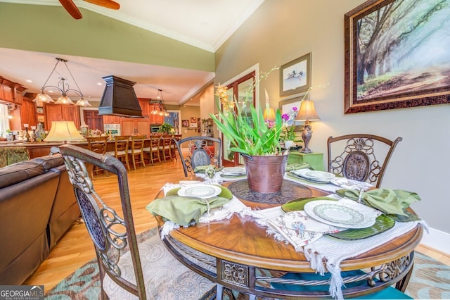 dining space featuring crown molding, a chandelier, vaulted ceiling, and light wood-type flooring