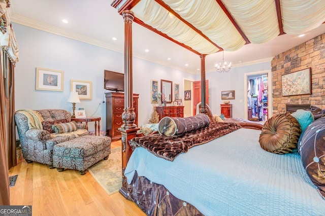 bedroom featuring ornate columns, ornamental molding, hardwood / wood-style flooring, a notable chandelier, and a stone fireplace