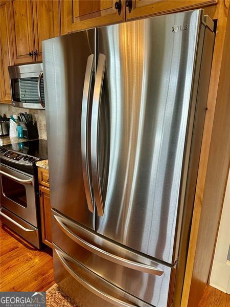 kitchen featuring tasteful backsplash, light stone countertops, appliances with stainless steel finishes, and light hardwood / wood-style flooring