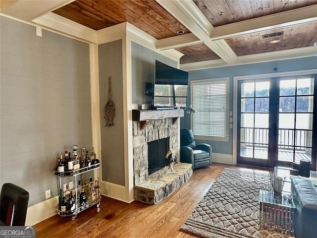 living room featuring coffered ceiling, crown molding, wood-type flooring, beam ceiling, and a stone fireplace