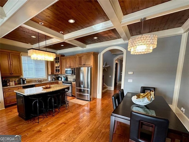 kitchen with a breakfast bar, appliances with stainless steel finishes, decorative light fixtures, a kitchen island, and light stone counters