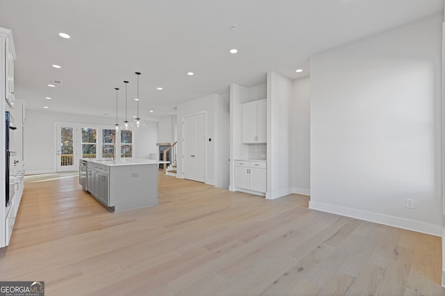 kitchen with white cabinets, decorative light fixtures, light wood-type flooring, and an island with sink