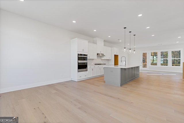 kitchen featuring pendant lighting, a center island with sink, light hardwood / wood-style floors, white cabinetry, and gas cooktop