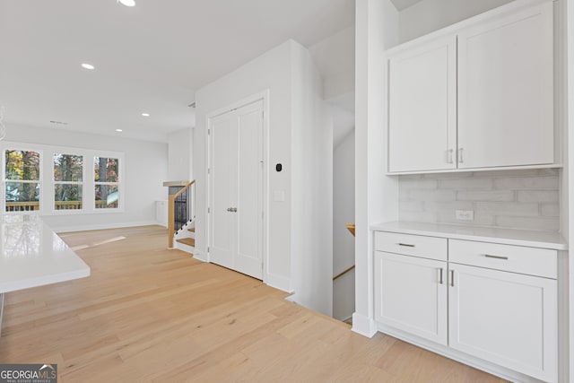 bar featuring light wood-type flooring, white cabinetry, and backsplash