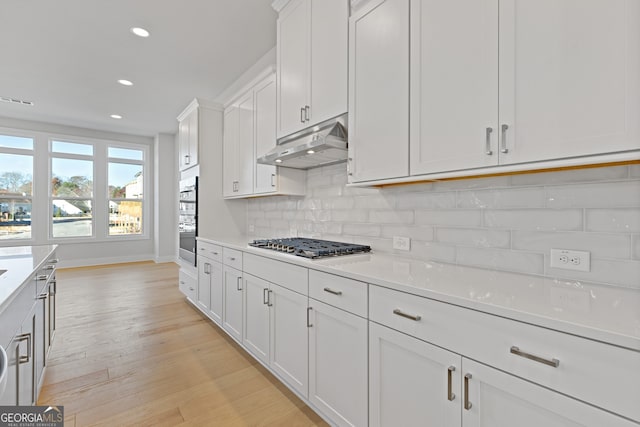 kitchen with appliances with stainless steel finishes, light wood-type flooring, white cabinetry, and backsplash