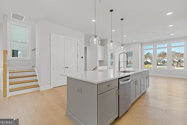 kitchen with pendant lighting, stainless steel dishwasher, a kitchen island with sink, and sink