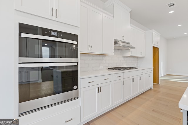 kitchen with white cabinets, appliances with stainless steel finishes, light wood-type flooring, and tasteful backsplash