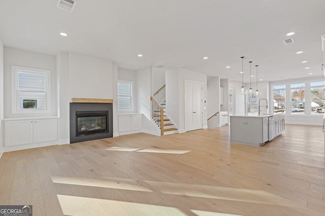 unfurnished living room featuring a tiled fireplace, sink, and light hardwood / wood-style floors