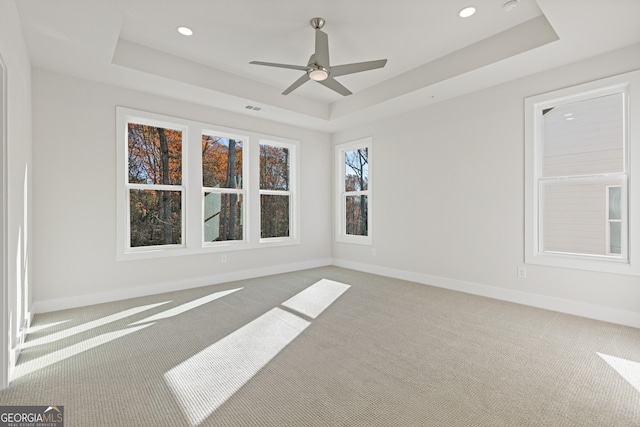 carpeted empty room with a raised ceiling and ceiling fan