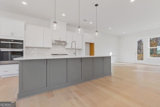 kitchen with decorative light fixtures, a spacious island, white cabinetry, and light hardwood / wood-style flooring