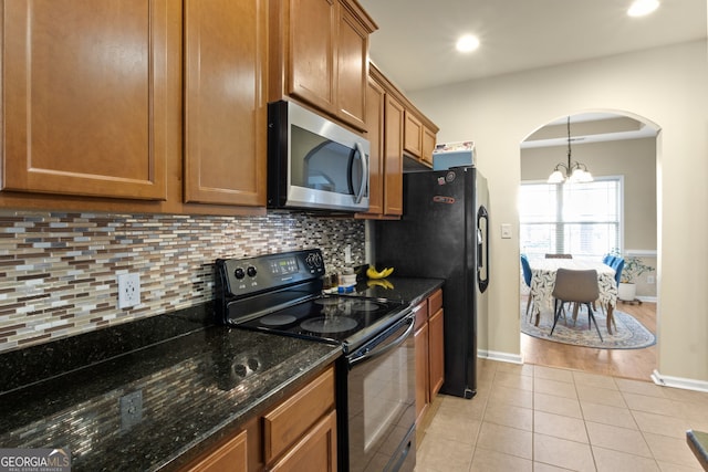 kitchen with light hardwood / wood-style flooring, a notable chandelier, dark stone countertops, decorative light fixtures, and black appliances