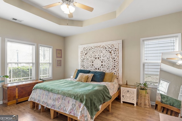 bedroom with light hardwood / wood-style floors, a raised ceiling, and ceiling fan