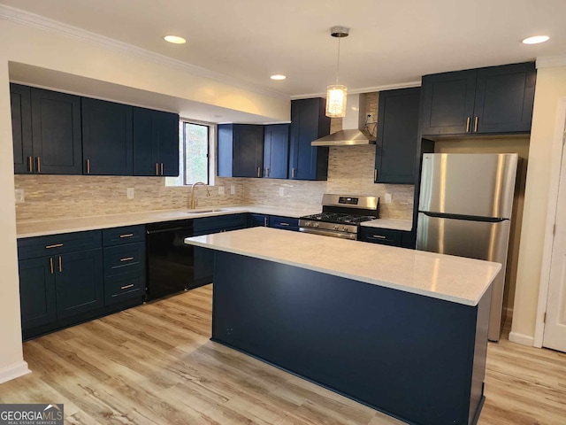 kitchen featuring wall chimney range hood, sink, hanging light fixtures, appliances with stainless steel finishes, and light hardwood / wood-style floors