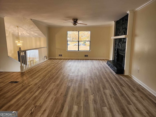 unfurnished living room with ceiling fan with notable chandelier, a stone fireplace, wood-type flooring, and crown molding