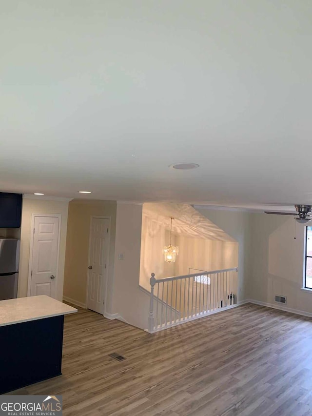 unfurnished living room featuring ceiling fan with notable chandelier and wood-type flooring