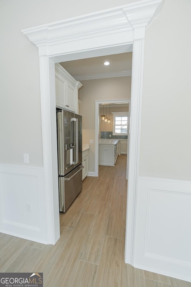 kitchen with high quality fridge, white cabinetry, crown molding, and light wood-type flooring