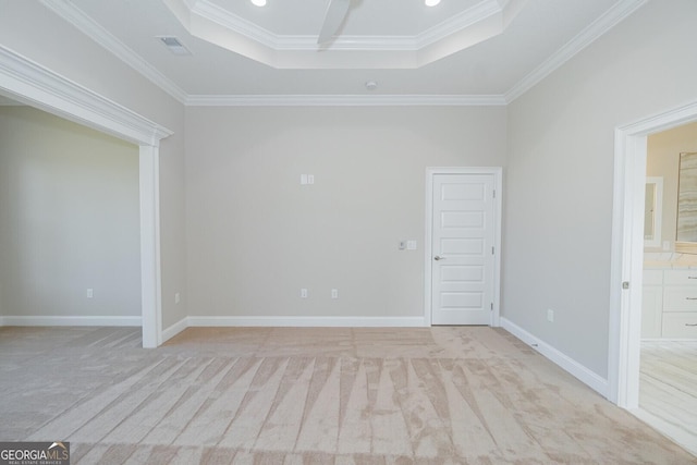 empty room featuring a tray ceiling, crown molding, and light colored carpet