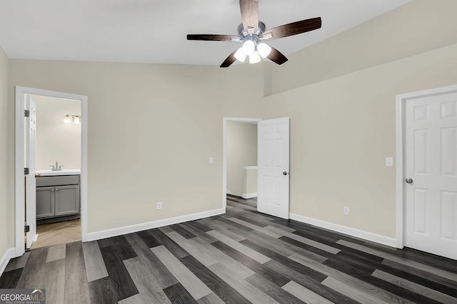 unfurnished bedroom featuring ensuite bathroom, baseboards, a sink, dark wood-style floors, and vaulted ceiling