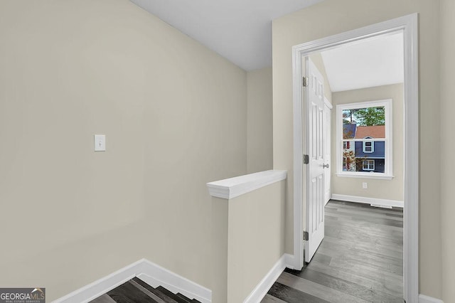 hall with wood finished floors, baseboards, and an upstairs landing