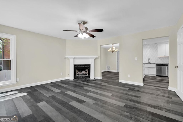 unfurnished living room with dark wood-type flooring, baseboards, a fireplace with flush hearth, and ceiling fan with notable chandelier