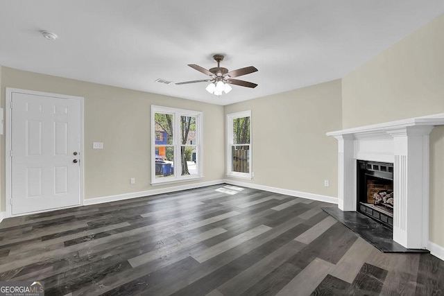 unfurnished living room with baseboards, dark wood-type flooring, a fireplace with raised hearth, visible vents, and ceiling fan