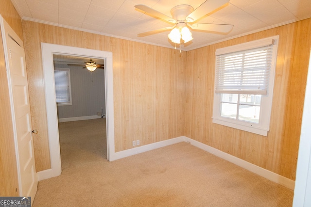 spare room featuring carpet, crown molding, ceiling fan, and wooden walls