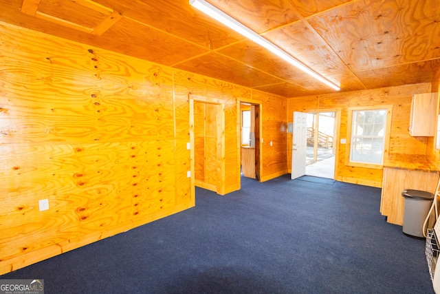 spare room featuring wooden walls and dark carpet