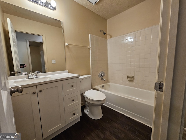 full bathroom featuring hardwood / wood-style floors, vanity, tiled shower / bath, toilet, and a textured ceiling