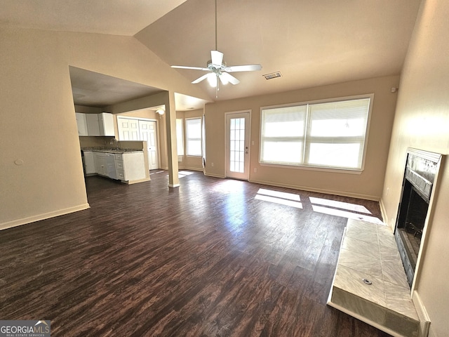 unfurnished living room featuring dark wood-type flooring, a tile fireplace, sink, vaulted ceiling, and ceiling fan