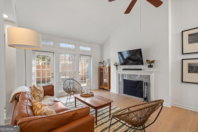 living room featuring high vaulted ceiling, light wood-style flooring, a high end fireplace, and baseboards