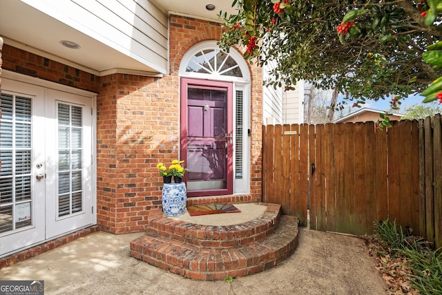 property entrance featuring french doors, brick siding, and fence