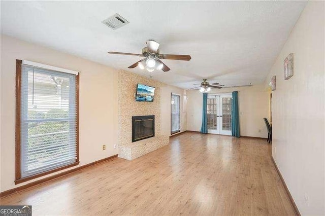 unfurnished living room featuring ceiling fan, light wood-type flooring, a fireplace, and french doors