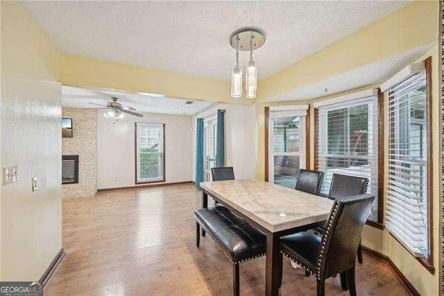 dining room featuring hardwood / wood-style flooring, ceiling fan with notable chandelier, a large fireplace, and a textured ceiling