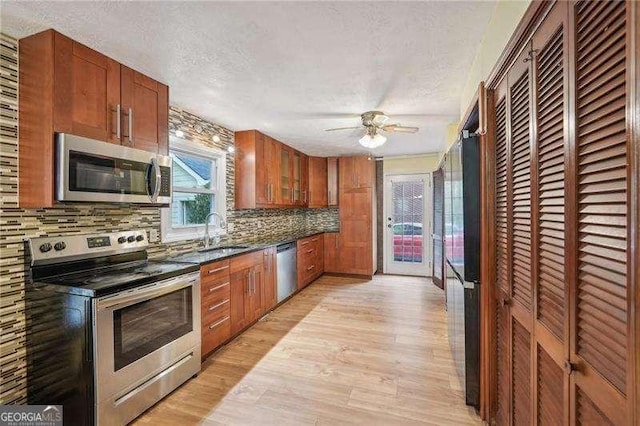 kitchen with sink, backsplash, a textured ceiling, appliances with stainless steel finishes, and light wood-type flooring