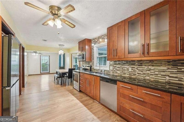 kitchen featuring stainless steel appliances, sink, light hardwood / wood-style flooring, dark stone countertops, and hanging light fixtures