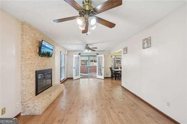 unfurnished living room featuring ceiling fan, a fireplace, wood-type flooring, and french doors