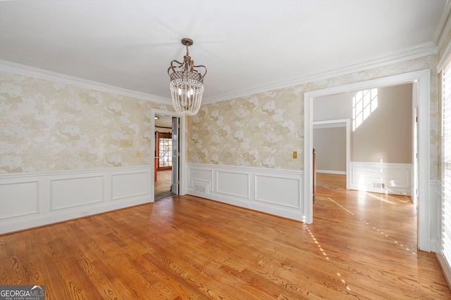 spare room featuring light hardwood / wood-style flooring, ornamental molding, and a notable chandelier